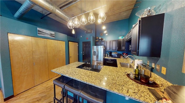 kitchen featuring black electric stovetop, a high ceiling, a sink, a peninsula, and stainless steel fridge with ice dispenser