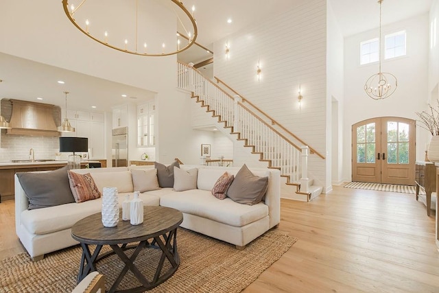 living room with a notable chandelier, french doors, stairway, light wood-type flooring, and a wealth of natural light