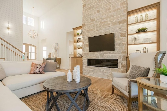 living area with stairway, a stone fireplace, a high ceiling, and wood finished floors