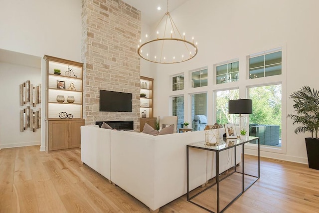 living room with a notable chandelier, a fireplace, a high ceiling, light wood-style floors, and baseboards