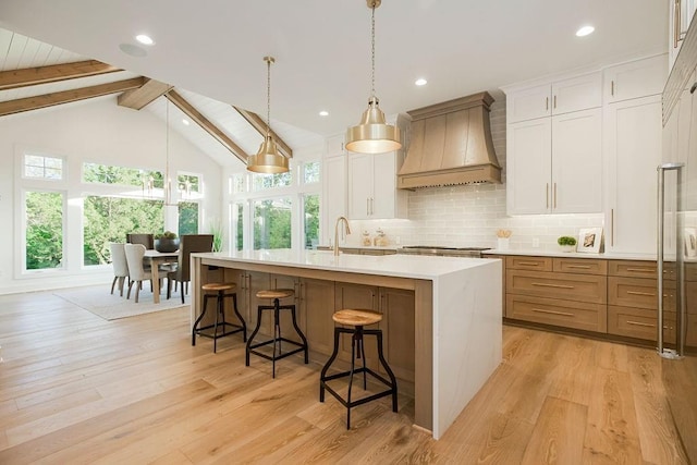 kitchen with tasteful backsplash, premium range hood, light wood-style floors, and an island with sink