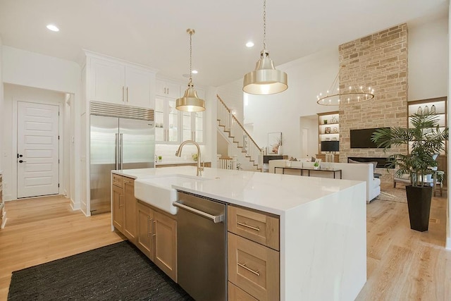 kitchen with appliances with stainless steel finishes, a kitchen island with sink, a sink, and light wood-style flooring