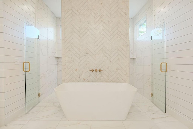 full bathroom featuring marble finish floor, a soaking tub, a shower stall, and tile walls