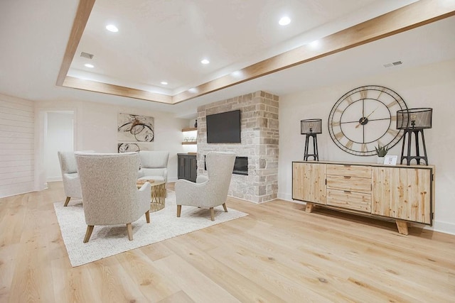 living room with a stone fireplace, wood finished floors, a raised ceiling, and recessed lighting