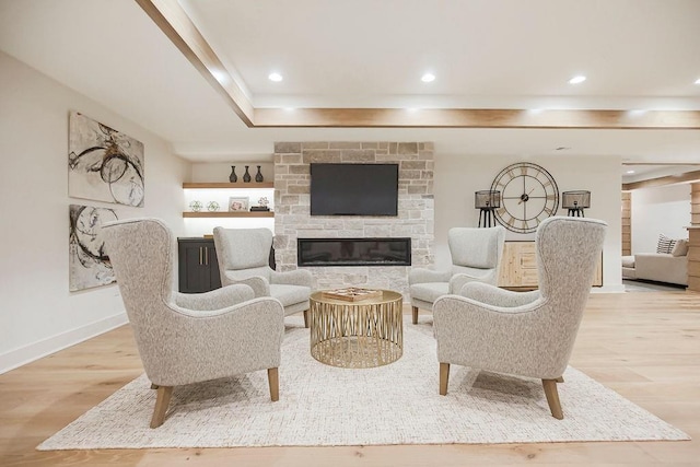 living area with baseboards, a stone fireplace, light wood-type flooring, and recessed lighting