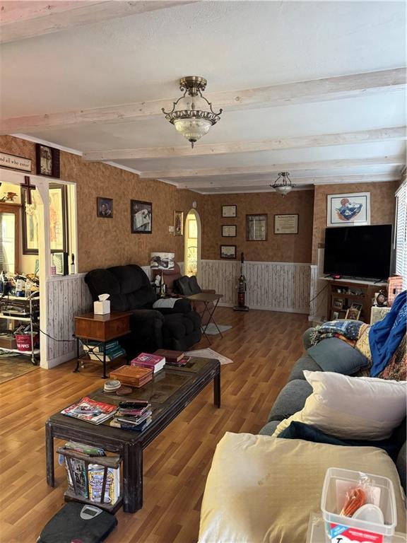 living area with wallpapered walls, beamed ceiling, and wood finished floors