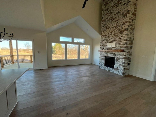 unfurnished living room featuring a healthy amount of sunlight, a high ceiling, wood finished floors, and a stone fireplace