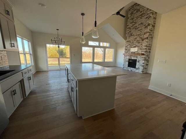 kitchen with open floor plan, high vaulted ceiling, a stone fireplace, and wood finished floors