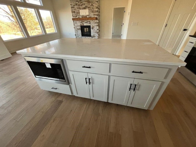 kitchen featuring a fireplace, light wood finished floors, light countertops, open floor plan, and white cabinetry