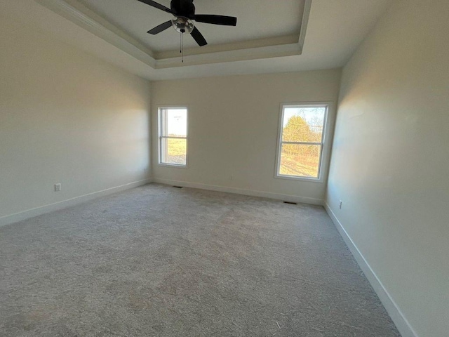 carpeted empty room featuring a tray ceiling, visible vents, ceiling fan, and baseboards