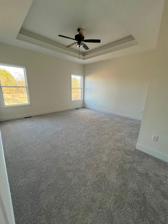 empty room with a ceiling fan, baseboards, a tray ceiling, and carpet flooring