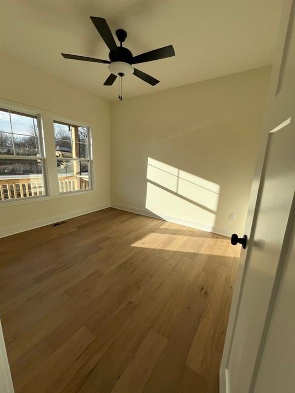 unfurnished room featuring a ceiling fan, wood finished floors, visible vents, and baseboards