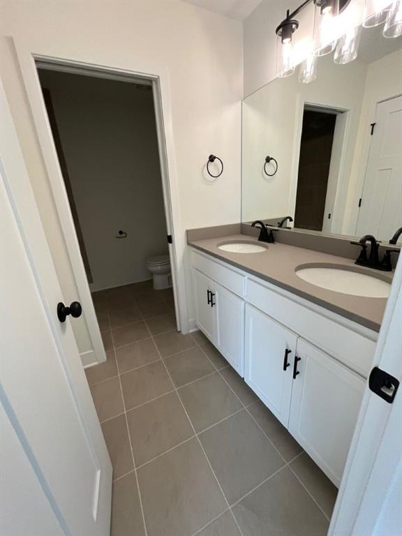 bathroom featuring double vanity, a sink, toilet, and tile patterned floors