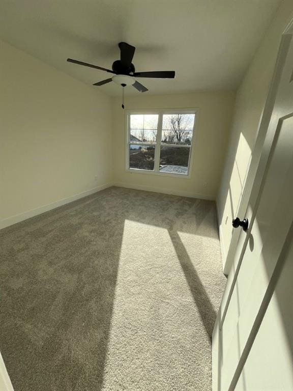 carpeted spare room featuring a ceiling fan and baseboards