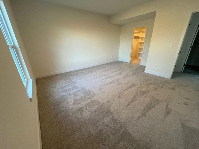 unfurnished bedroom with carpet, a closet, a spacious closet, and baseboards