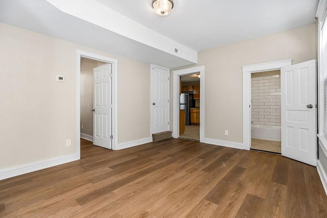 unfurnished bedroom featuring baseboards, wood finished floors, and freestanding refrigerator