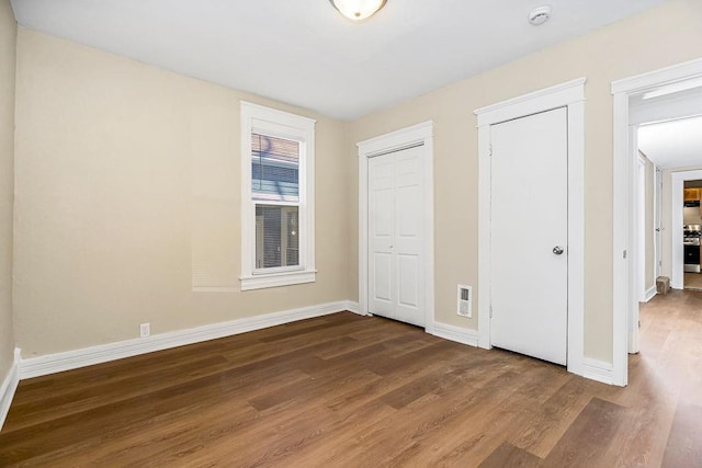 unfurnished bedroom with visible vents, two closets, baseboards, and wood finished floors