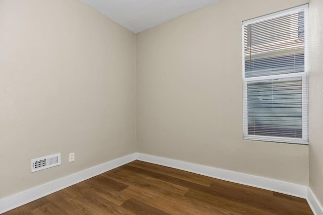 spare room featuring dark wood-style flooring, visible vents, and baseboards