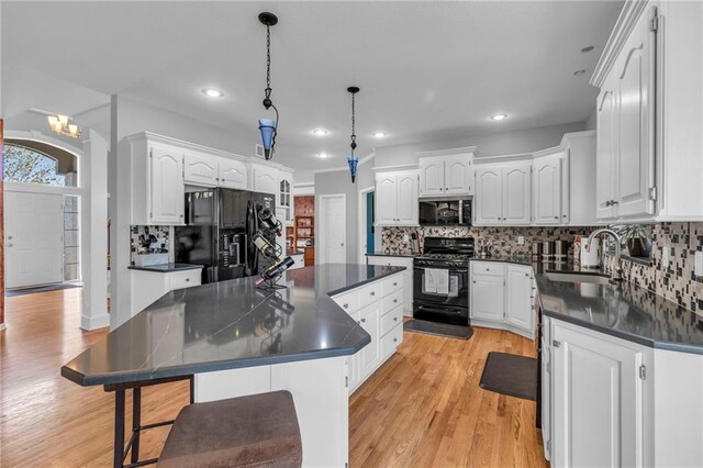 kitchen with black appliances, a sink, dark countertops, a center island, and white cabinets