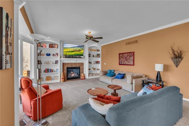 living area featuring carpet flooring, a ceiling fan, a tile fireplace, built in features, and crown molding