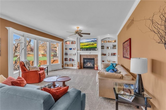 living area featuring crown molding, light carpet, a ceiling fan, a tile fireplace, and built in features