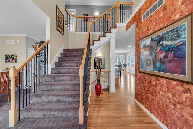 staircase featuring wood finished floors, baseboards, ornamental molding, and a high ceiling