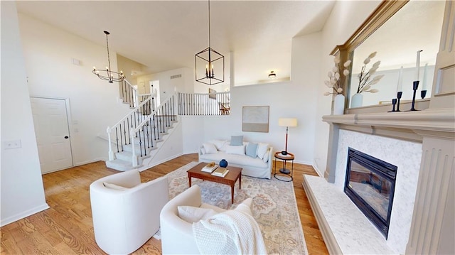 living room with baseboards, stairway, wood finished floors, a fireplace, and a notable chandelier