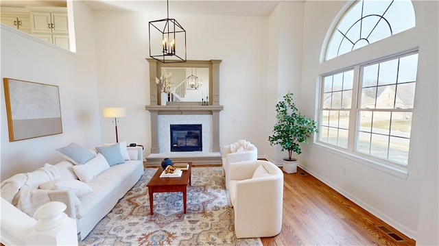 living room with visible vents, a glass covered fireplace, a towering ceiling, light wood-style flooring, and a chandelier