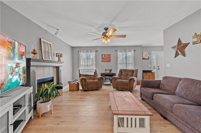 living room featuring light wood-type flooring, a textured ceiling, ceiling fan, and a tiled fireplace