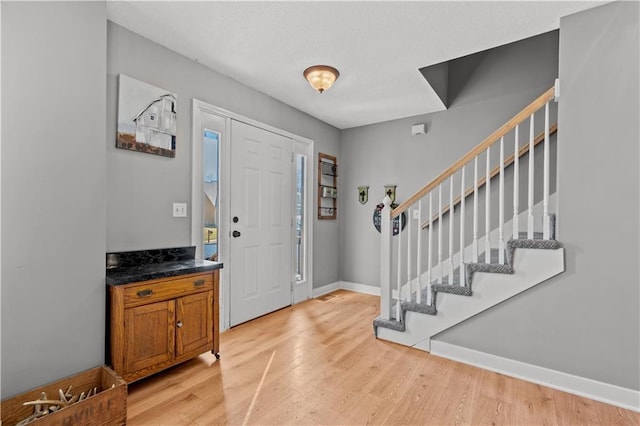 foyer featuring stairs, light wood-type flooring, and baseboards