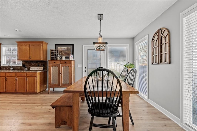 dining area with baseboards, a textured ceiling, a healthy amount of sunlight, and light wood-style flooring