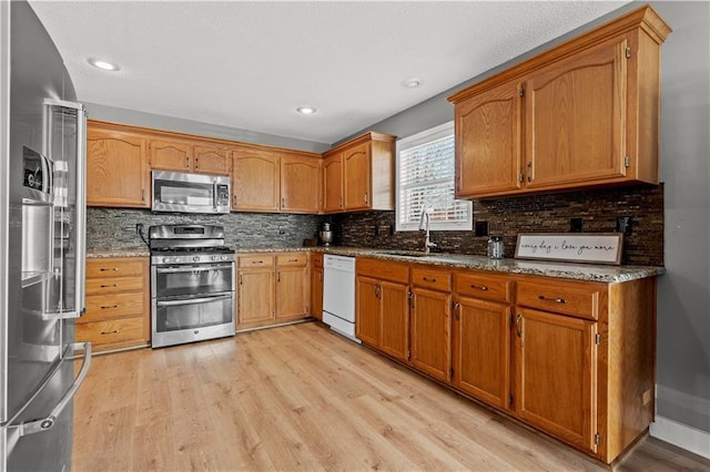 kitchen with stone counters, stainless steel appliances, light wood-style floors, and a sink