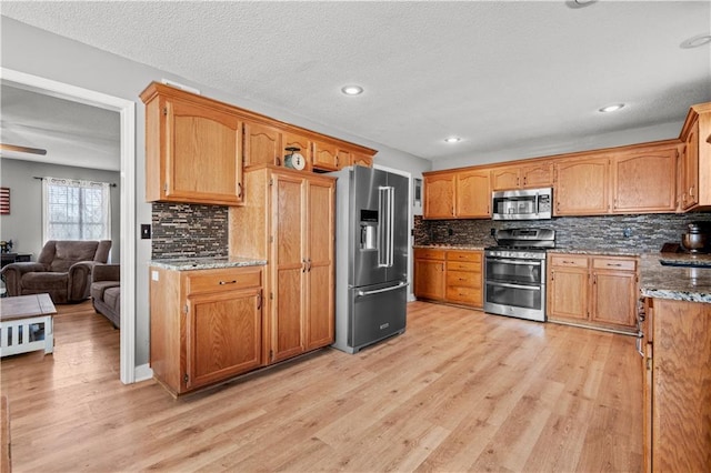 kitchen featuring decorative backsplash, light wood-style flooring, stone countertops, and appliances with stainless steel finishes