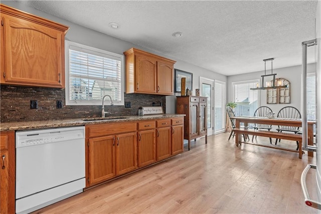 kitchen featuring light wood-type flooring, a sink, tasteful backsplash, brown cabinetry, and white dishwasher