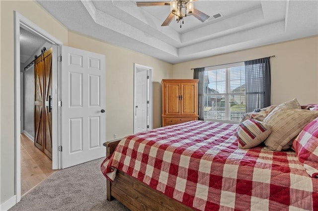 bedroom with a ceiling fan, visible vents, a barn door, light carpet, and a raised ceiling