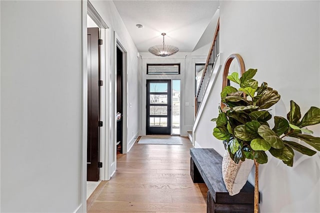 foyer entrance with stairs, light wood-type flooring, baseboards, and an inviting chandelier