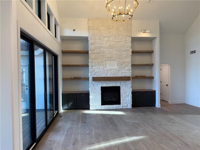 unfurnished living room with a stone fireplace, wood finished floors, a towering ceiling, visible vents, and an inviting chandelier