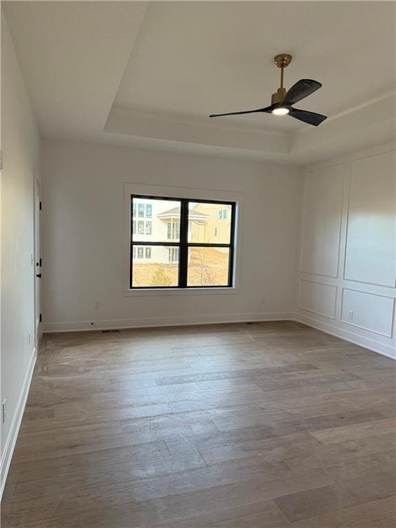 unfurnished room with a tray ceiling, a decorative wall, and wood finished floors