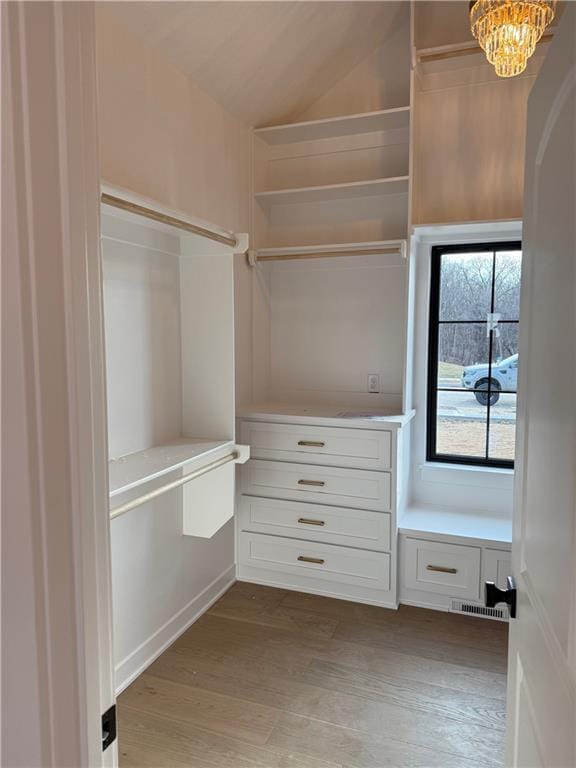 walk in closet with vaulted ceiling, light wood finished floors, visible vents, and a notable chandelier