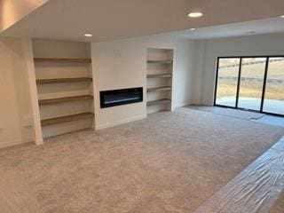 unfurnished living room featuring carpet, a glass covered fireplace, baseboards, and recessed lighting