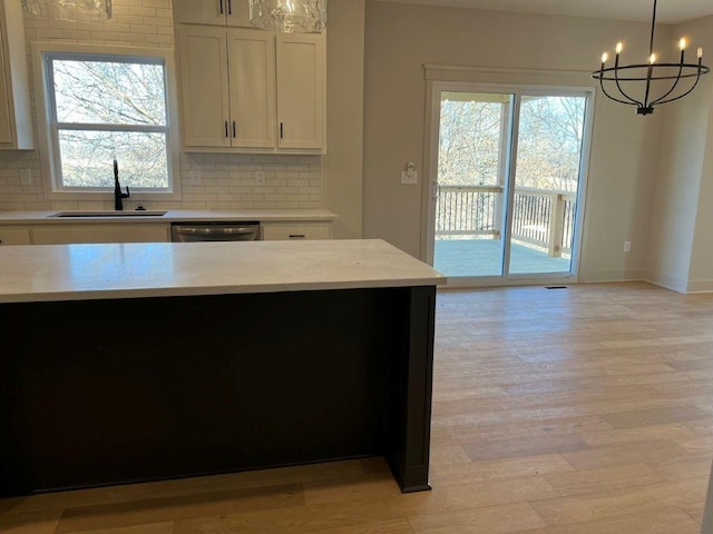 kitchen featuring tasteful backsplash, white cabinets, a sink, light wood-type flooring, and stainless steel dishwasher