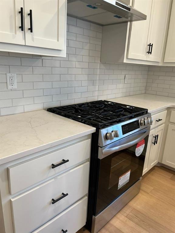 kitchen featuring under cabinet range hood, white cabinets, light wood-style floors, tasteful backsplash, and stainless steel range with gas stovetop