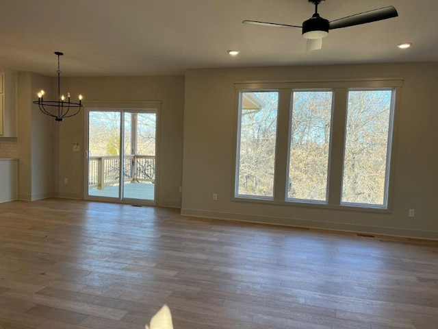 interior space with baseboards, wood finished floors, and ceiling fan with notable chandelier