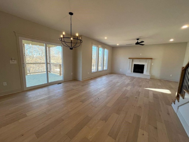 unfurnished living room featuring a fireplace with raised hearth, light wood finished floors, ceiling fan with notable chandelier, and baseboards