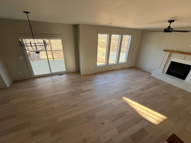 unfurnished living room with visible vents, a premium fireplace, light wood-style floors, baseboards, and ceiling fan with notable chandelier