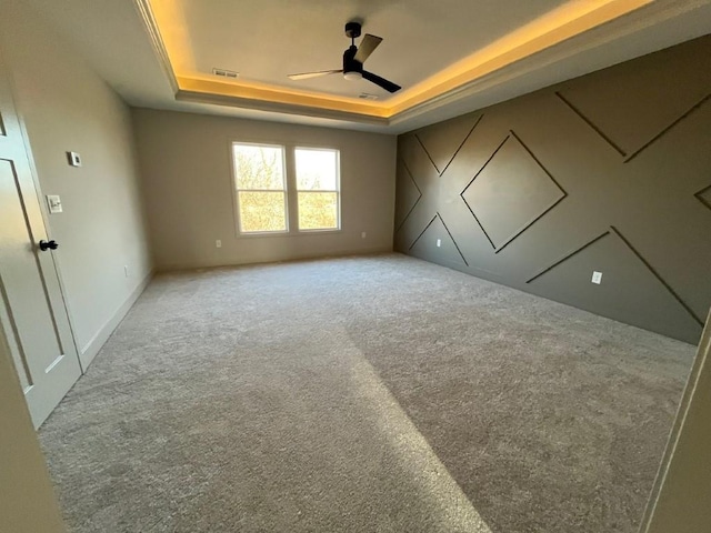 empty room with visible vents, carpet flooring, a raised ceiling, and a ceiling fan