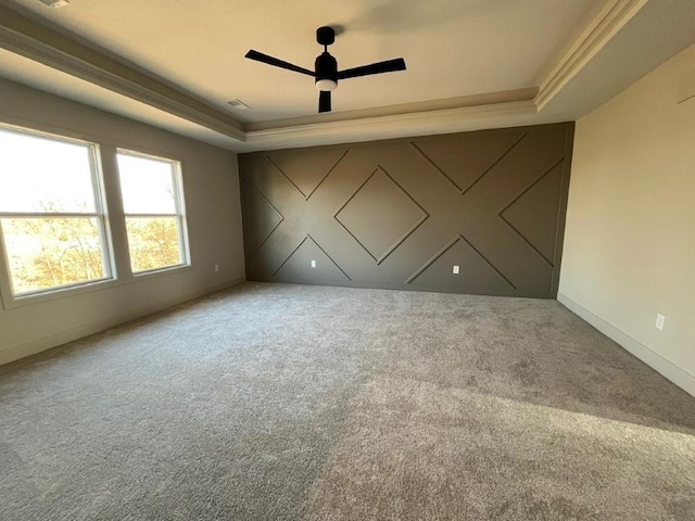 carpeted spare room with a tray ceiling, a ceiling fan, and baseboards