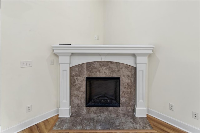 interior details featuring wood finished floors, a tile fireplace, and baseboards