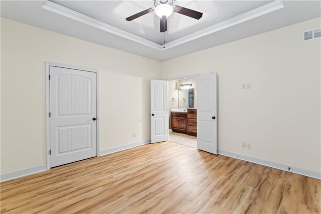 empty room featuring light wood-style floors, a raised ceiling, and crown molding