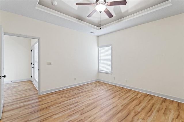 unfurnished room with ornamental molding, a tray ceiling, baseboards, and light wood-style floors